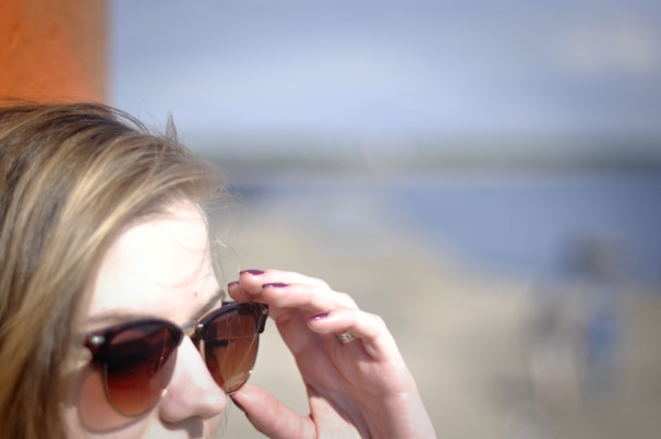 Side profile of a person adjusting their polarized sunglasses with a scenic outdoor background.