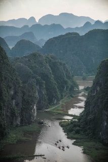 Peaceful river winding through the lush green karst landscape of Ninh Binh, with small boats carrying travelers under rocky cliffs.