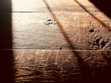 Warm, textured wooden floorboards with visible grain and shadows cast diagonally across the surface, creating a contrast between light and dark areas.