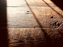 Warm, textured wooden floorboards with visible grain and shadows cast diagonally across the surface, creating a contrast between light and dark areas.