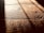 Warm, textured wooden floorboards with visible grain and shadows cast diagonally across the surface, creating a contrast between light and dark areas.