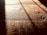 Warm, textured wooden floorboards with visible grain and shadows cast diagonally across the surface, creating a contrast between light and dark areas.