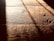 Warm, textured wooden floorboards with visible grain and shadows cast diagonally across the surface, creating a contrast between light and dark areas.