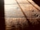Warm, textured wooden floorboards with visible grain and shadows cast diagonally across the surface, creating a contrast between light and dark areas.