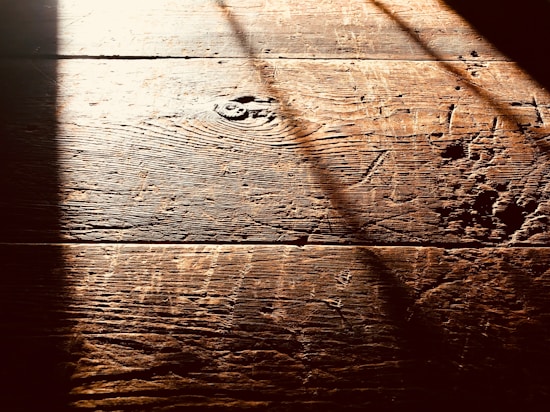 Warm, textured wooden floorboards with visible grain and shadows cast diagonally across the surface, creating a contrast between light and dark areas.