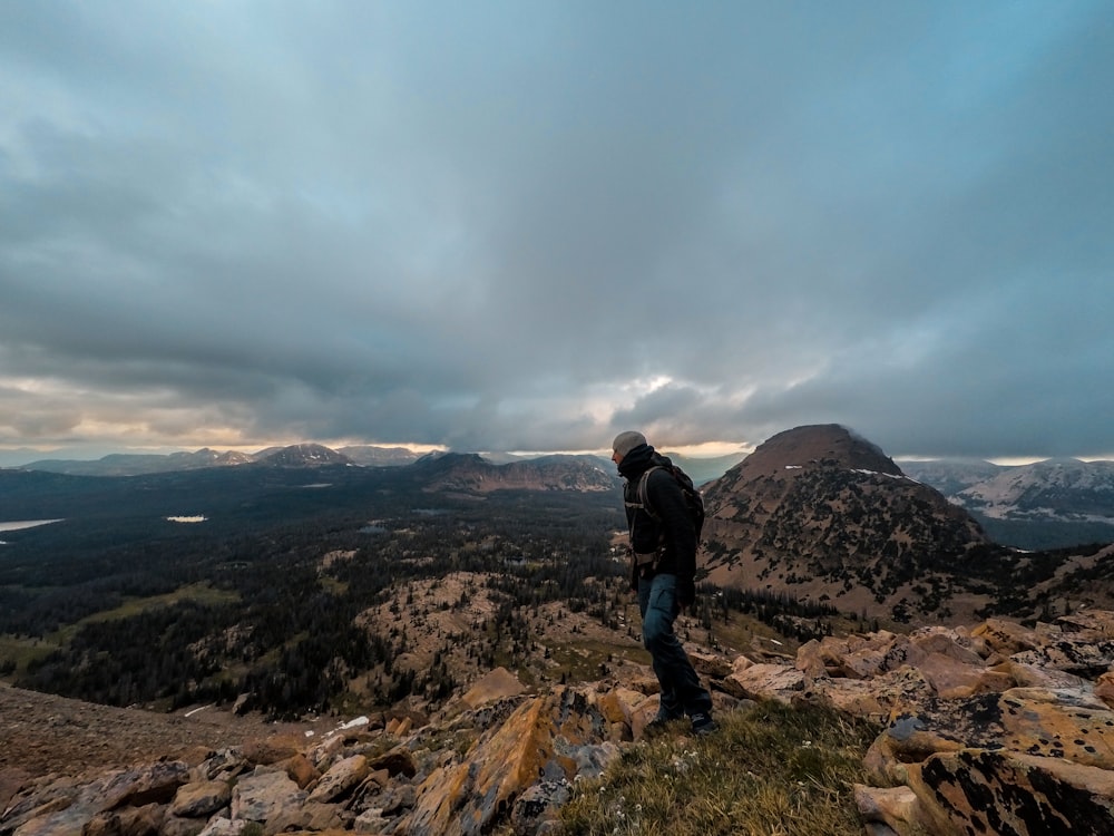 man standing on rocky mountain under gray cloudy sky