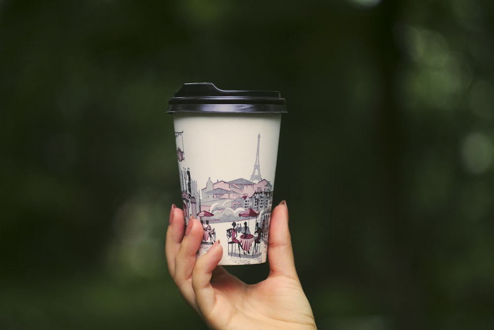 Persona che tiene la tazza di caffè usa e getta bianca e nera