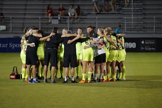 A vibrant soccer team huddled together on a sunny field, showing unity and energy.