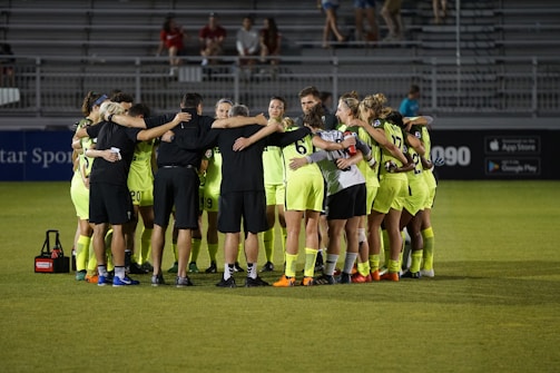 A vibrant soccer team huddled together on a sunny field, showing unity and energy.