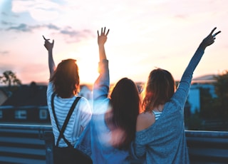 photo of three women lifting there hands \