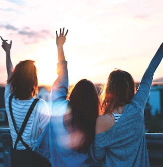 photo of three women lifting there hands \