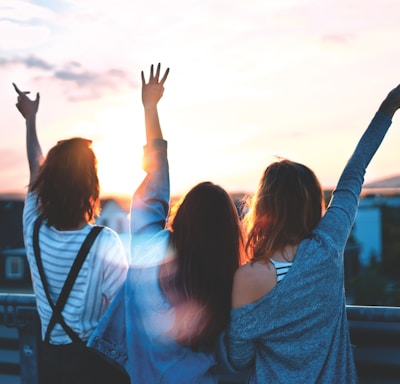 photo of three women lifting there hands \