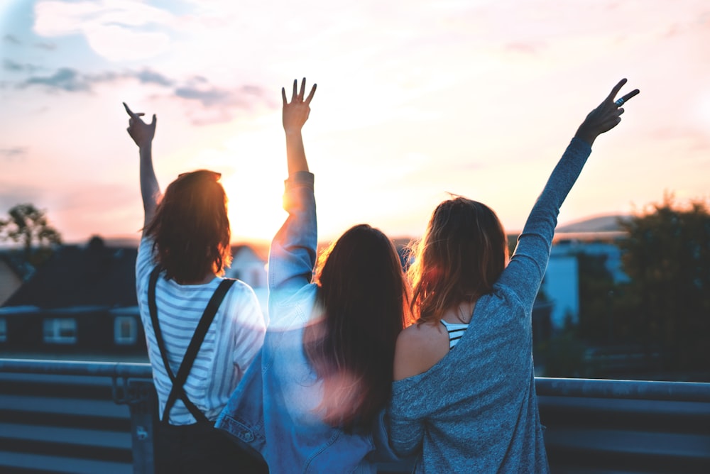 photo of three women lifting there hands \