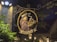 An illuminated sign hanging outside depicts a friar holding a tray piled with donuts. The sign reads 'The Donut Friar' and is artfully crafted with a circular design and ornamental ironwork. The backdrop is nighttime with ambient light from a nearby lamp post casting shadows.