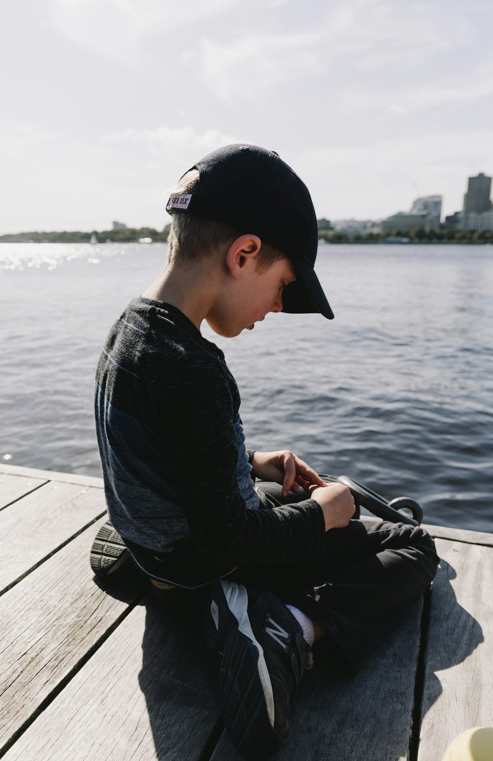 boy wearing black shirt and pants sitting on dock