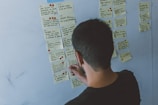 A smiling person happily sorting sticky notes on a corkboard shaped like a brain.