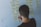 A person is organizing or affixing small sticky notes on a whiteboard. The notes contain various handwritten texts and some have small red dots on them. The person has short dark hair and is focusing on the task.