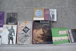 A collection of various books is arranged on a flat surface against a gray background. The books include titles on art, history, and biographies, featuring covers with illustrations of historical figures, artwork, and text in different languages.