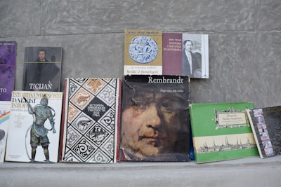 A collection of various books is arranged on a flat surface against a gray background. The books include titles on art, history, and biographies, featuring covers with illustrations of historical figures, artwork, and text in different languages.