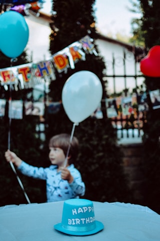 A happy child holding a printed party invitation with balloons and confetti in the background.