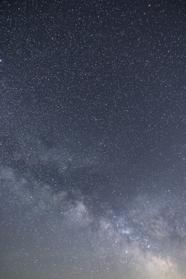 A starry night sky with a dense cluster of stars forming the Milky Way galaxy, spread across the center. The image captures a vast expanse of stars scattered against a dark backdrop.