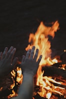 Close-up of hands around a campfire, glowing warmly against the night sky.