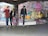 Three young men with skateboards are gathered in an urban environment filled with colorful graffiti. They stand on a concrete floor, and one of them is holding a bright pink skateboard. The walls and columns are covered in vibrant street art, creating a lively and edgy backdrop.
