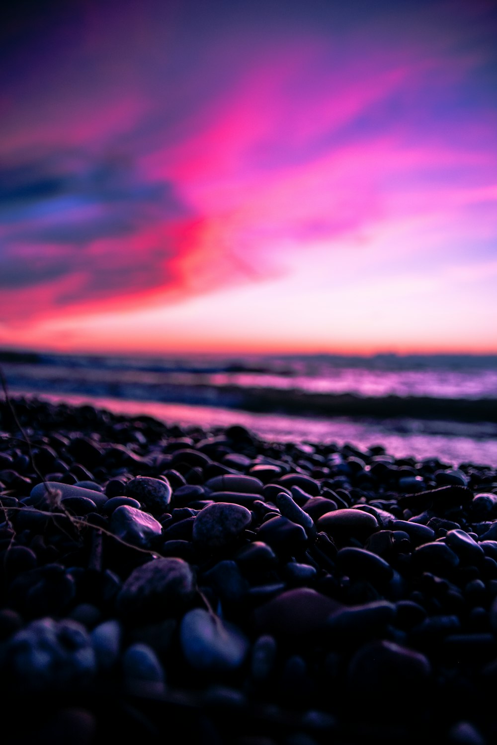 a beach with rocks and water under a colorful sky