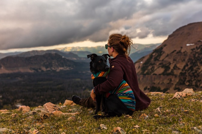 woman sitting beside black dog on mountain