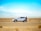 man standing beside white SUV near concrete road under blue sky at daytime