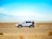 man standing beside white SUV near concrete road under blue sky at daytime