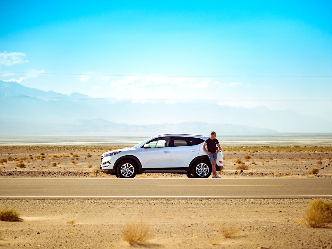 man standing beside white SUV near concrete road under blue sky at daytime