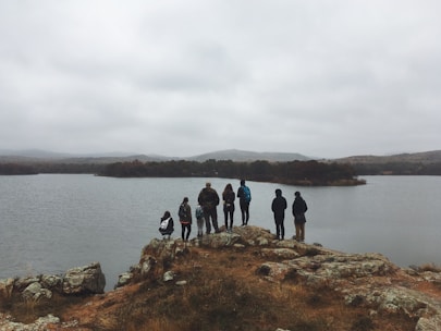A group of happy travelers standing beside a serene loch with rugged hills in the background.