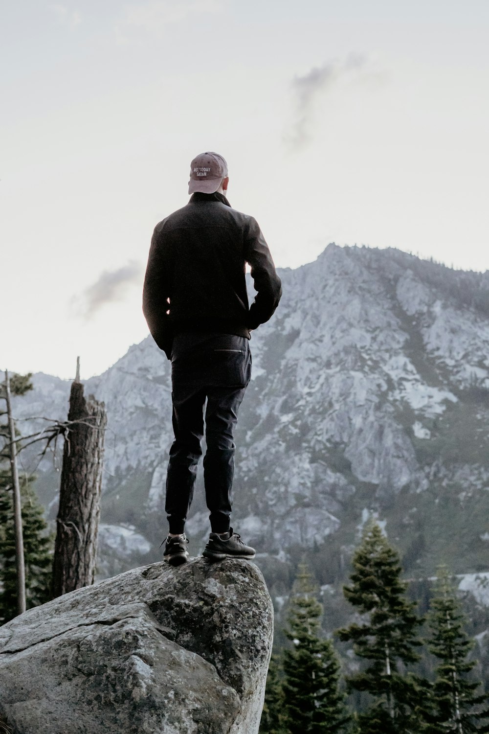 homme debout sur le rocher gris regardant le sommet de la montagne