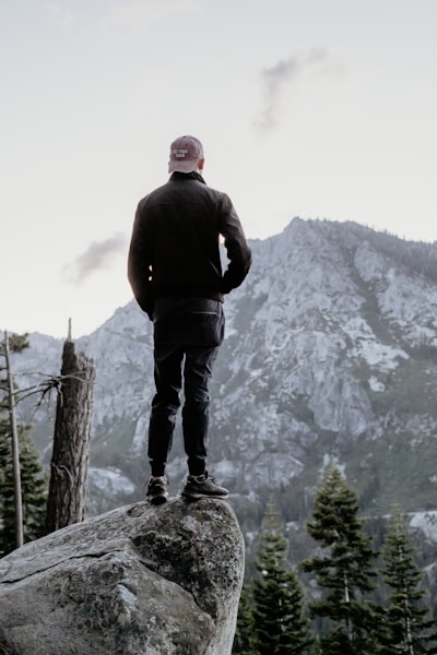 man standing on gray rock looking at mountain peak