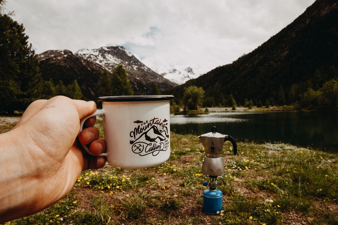 person holding white cup outdoors, Mountains are calling
