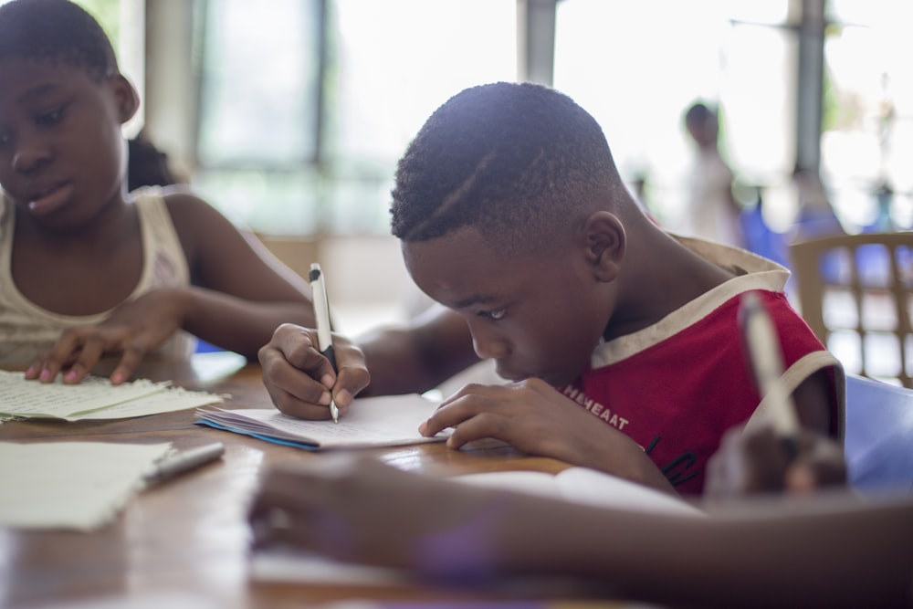 niño escribiendo en papel de impresora cerca de la niña