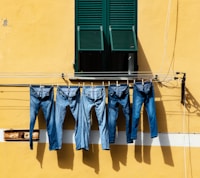 five blue denim jeans hanged on grey cable near window