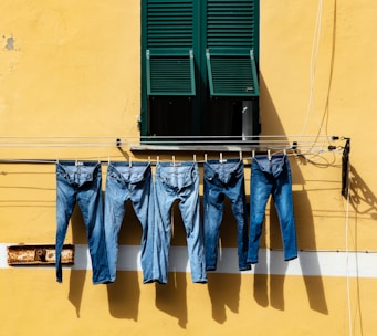 five blue denim jeans hanged on grey cable near window