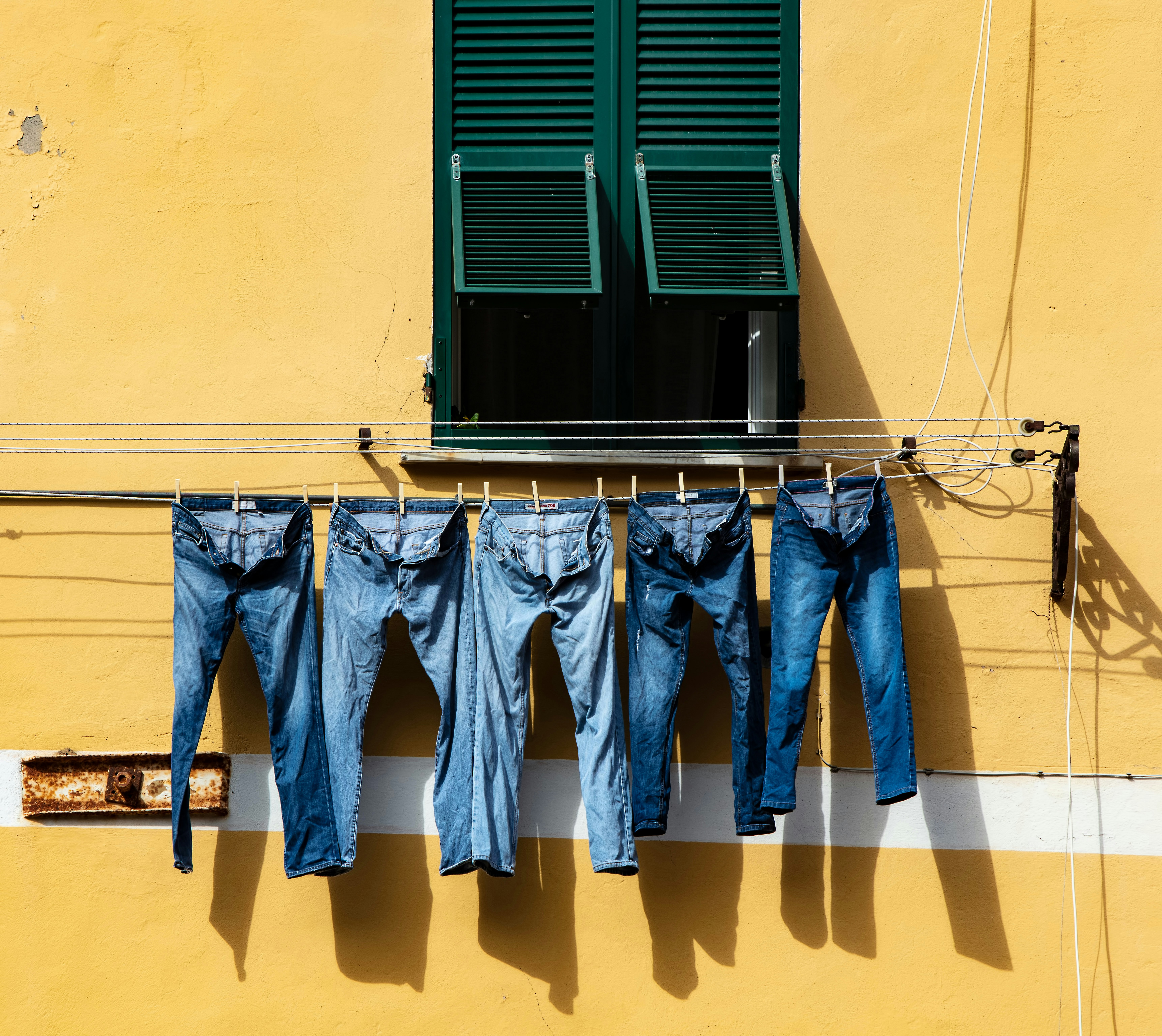 five blue denim jeans hanged on grey cable near window