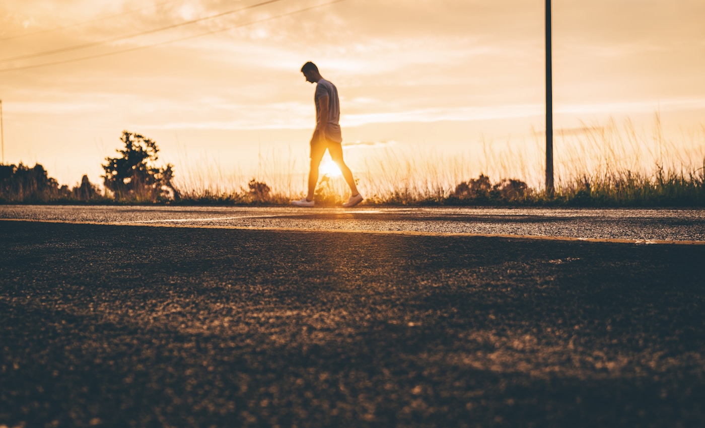 golden hour photography of man walking on asphalt road