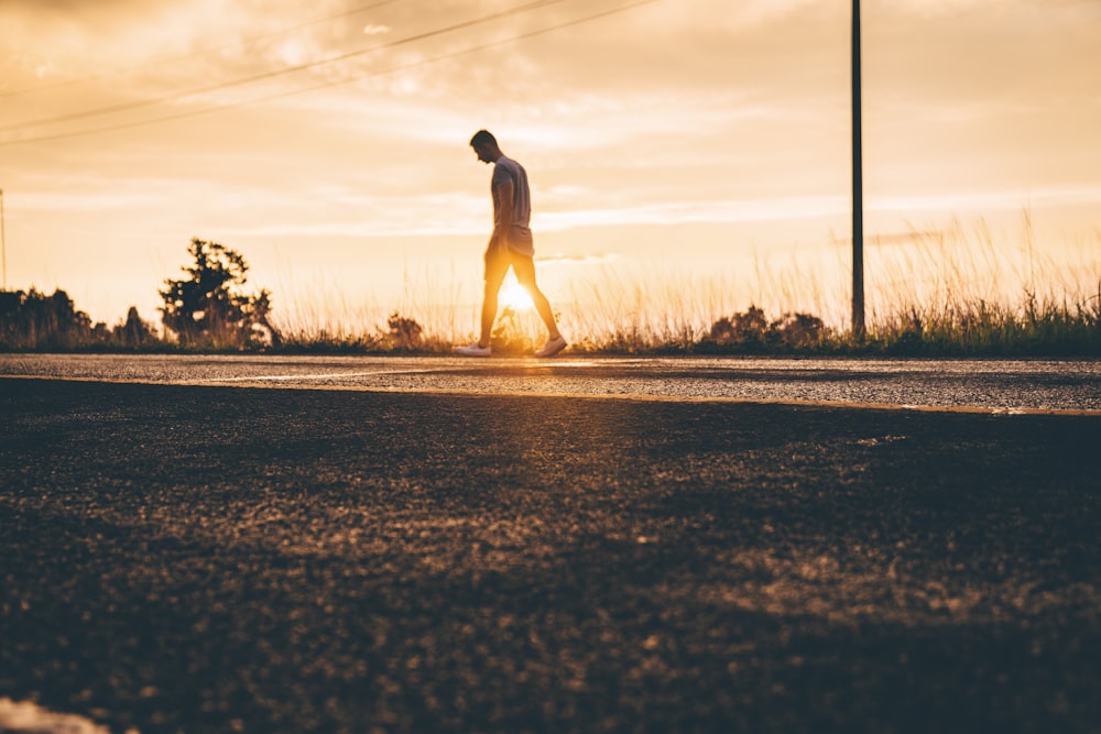 fotografia de hora de ouro do homem andando na estrada de asfalto