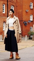 A model walking confidently down a sunlit street wearing a chic beige trench coat paired with tailored trousers.