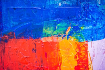 A vibrant abstract painting featuring bold and textured brush strokes. Dominant colors include vivid blues, rich reds, and bright yellows, blending and overlapping in a dynamic composition.