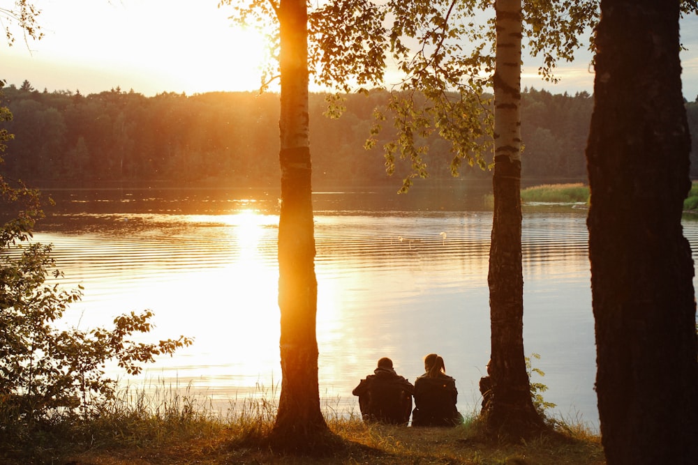 Homem e mulher sentados perto do corpo de água durante o pôr do sol