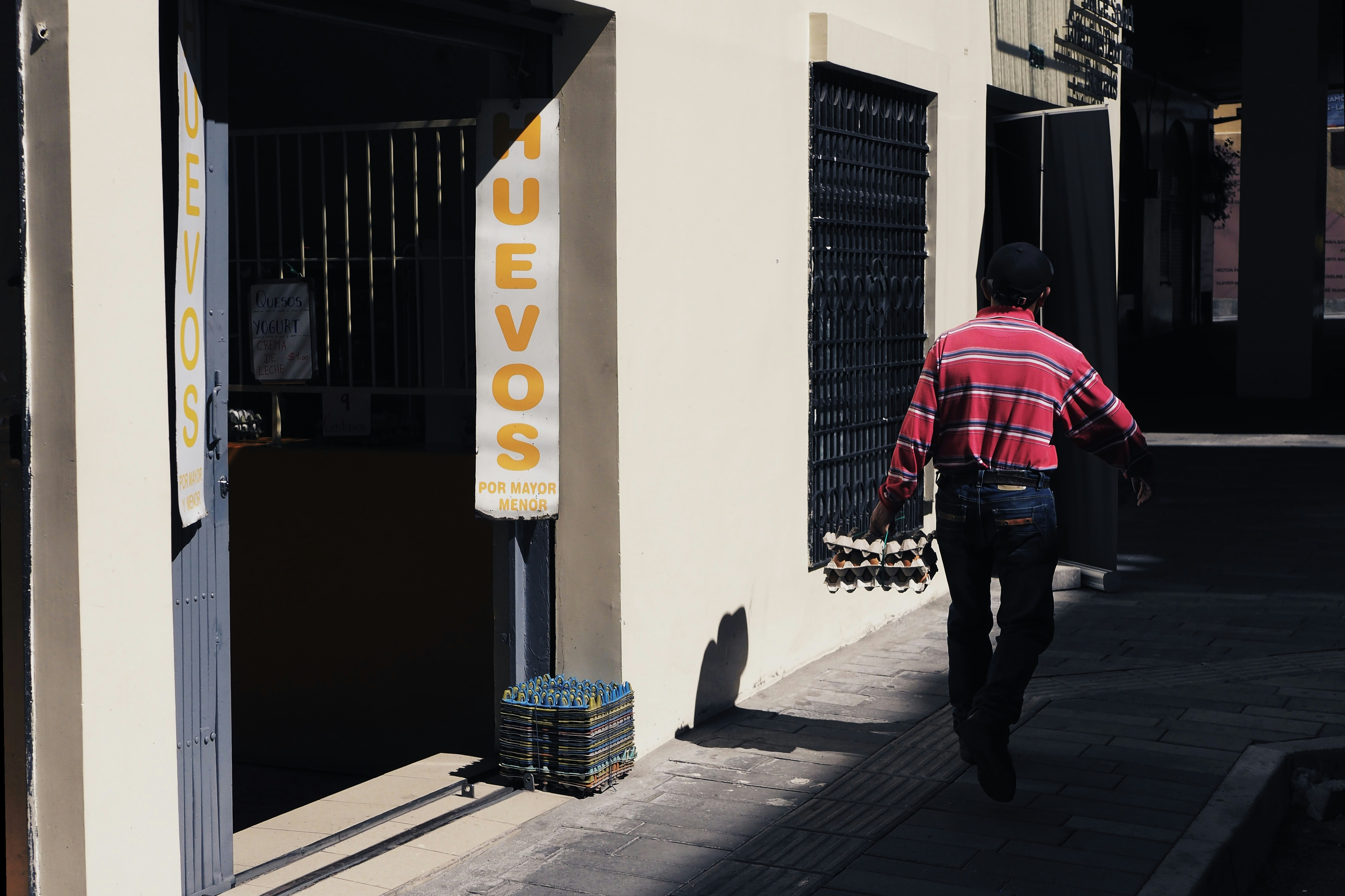 Scène de vie locale montrant un homme en rouge passant devant une maison colorée