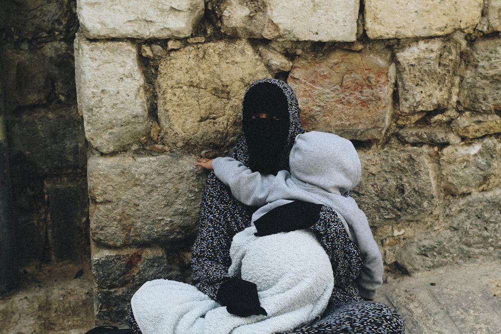 woman sitting on ground and leaning on wall hugging baby