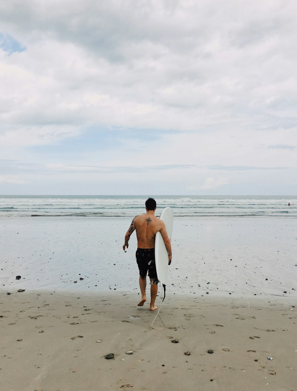 man in black shorts holding surfboard on beach