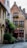 A quaint narrow street lined with old brick buildings, including a charming establishment with red-framed windows and a sign reading 'Vlaamsche Pot.' The façade is adorned with greenery and flowers. The cobblestone path and cozy outdoor seating evoke a sense of vintage European architecture.
