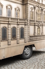 A mobile structure mimics the facade of a classical building with detailed architectural elements such as windows, columns, and ornate features. It is mounted on wheels, indicating it can be transported, and rests on a cobblestone surface.